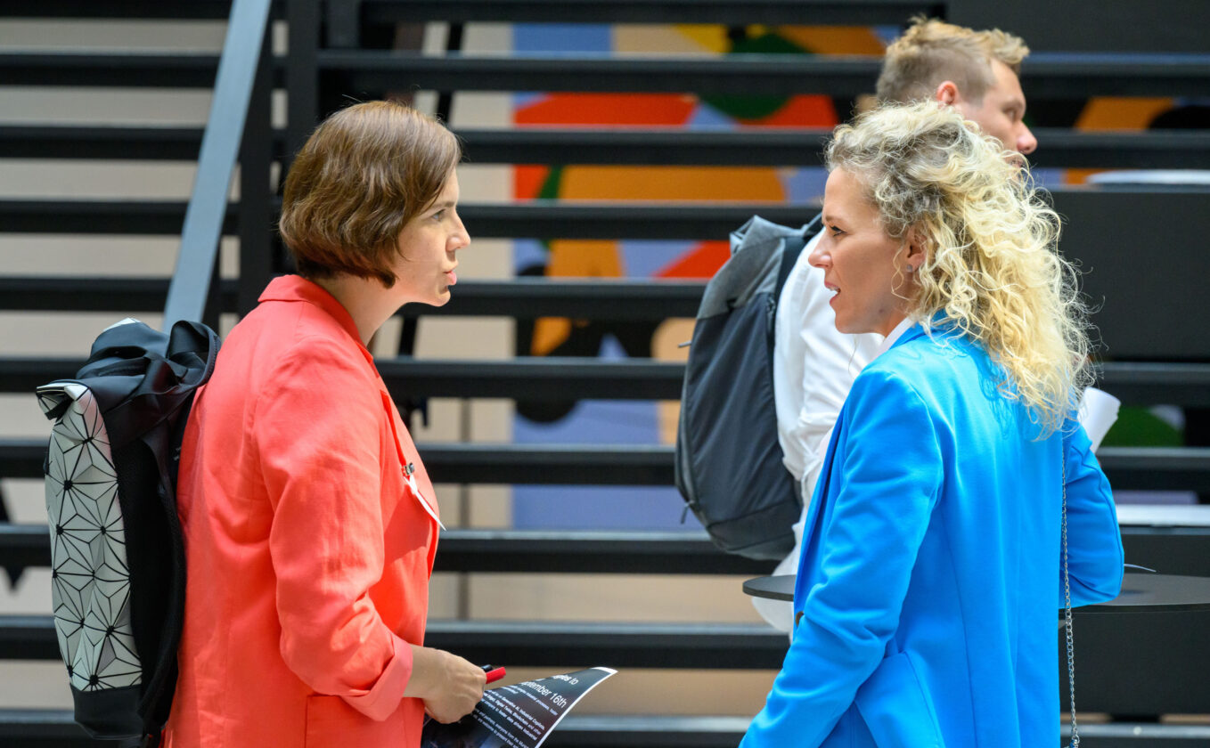 Two women discussing at an AI conference in front of stairs