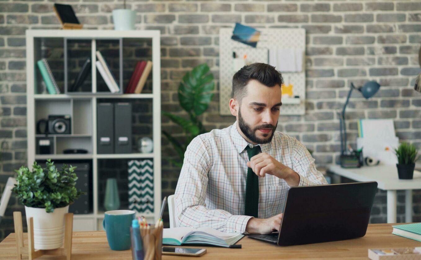 A man is sitting at his desk and works on his laptop.