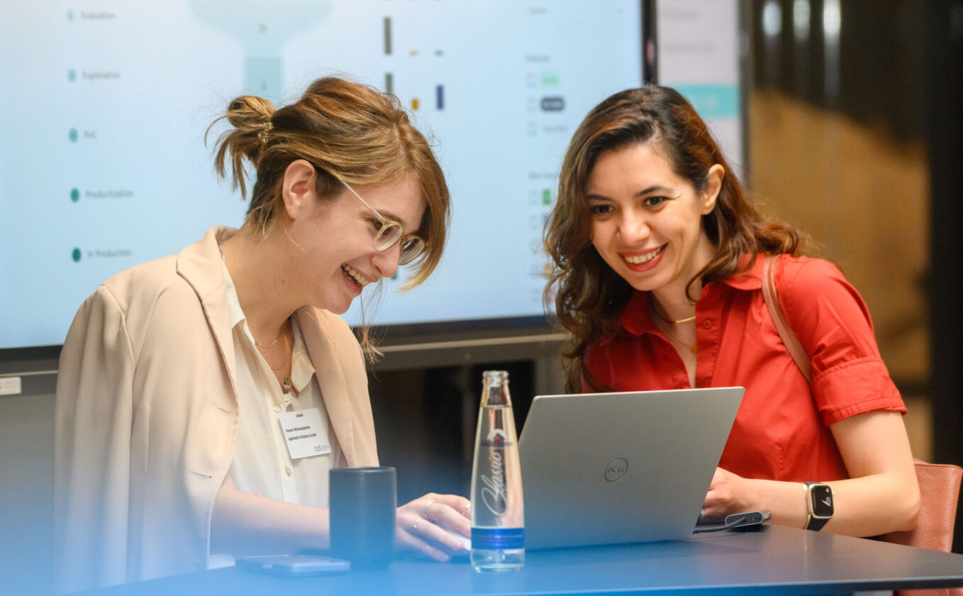 Two smiling women are looking at their laptop.