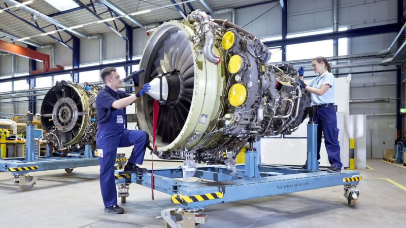 Zwei MechanikerInnen arbeiten an einer alleinstehenden Flugzeugturbine in einer Halle