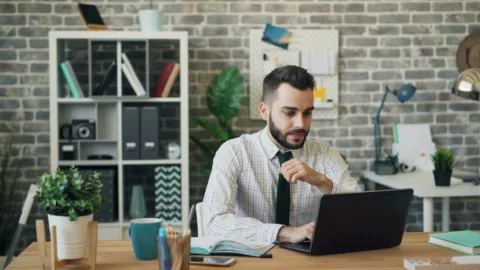 Ein Mann sitzt an seinem Schreibtisch und arbeitet an seinem Laptop