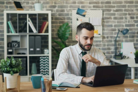 A man is sitting at his desk and works on his laptop.