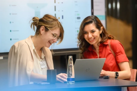 Two smiling women are looking at their laptop.