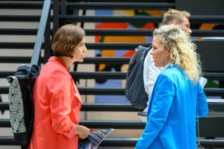 Two women discussing at an AI conference in front of stairs