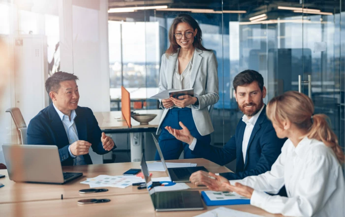 four people in a meeting room leading a discussion three sitting on a table one woman standing