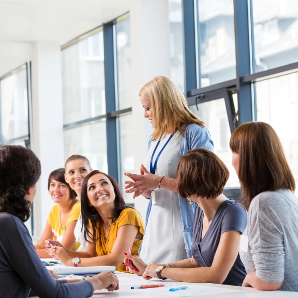 A female instructor explains something to a group of women who are sitting at a table.